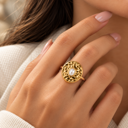 Gold-coloured oval ring with a textured frame and smooth white centre detail on a white background.