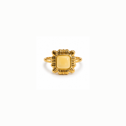 Gold-coloured square statement ring with a rounded pale yellow centre and ornate ridged decorative frame on a white background.